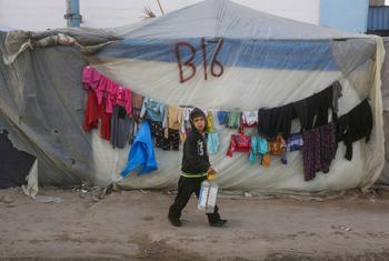 A young boy passes by a shelter on the way to collect water.