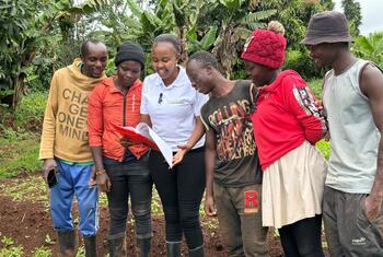 Maryanne Gichanga, entrepreneure agricole kenyane, dirige un groupe d'agriculteurs dans un champ, examinant les données des capteurs IoT et des images satellites pour améliorer la santé des cultures et les informations météorologiques.