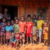 A group of children and a woman stand in front of a brick house in Bangassou, Central African Republic, during a press visit to assess the food crisis. The woman holds a bowl of grains, symbolizing emergency food assistance provided by the World Bank-funded PRUCAC project.