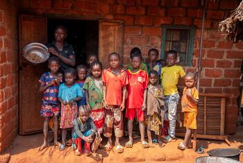 A group of children and a woman stand in front of a brick house in Bangassou, Central African Republic, during a press visit to assess the food crisis. The woman holds a bowl of grains, symbolizing emergency food assistance provided by the World Bank-funded PRUCAC project.