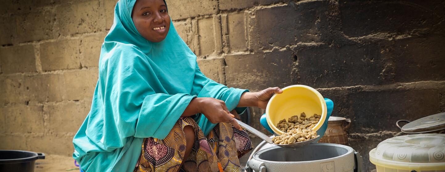 Fatsuma Jumani, mère de deux enfants à Gwio Kura, dans l'État de Yobe, au Nigeria, sourit alors qu'elle prépare de la nourriture, montrant son nouveau moyen de subsistance soutenu par le programme Cash-for-Work du PAM.