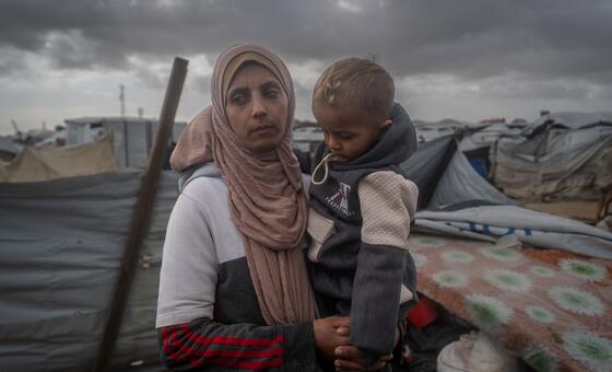 السيدة ياسمين - وهي أرملة فلسطينية - تحمل طفلها الصغير في موقع إيواء مؤقت في خان يونس، جنوب قطاع غزة. 