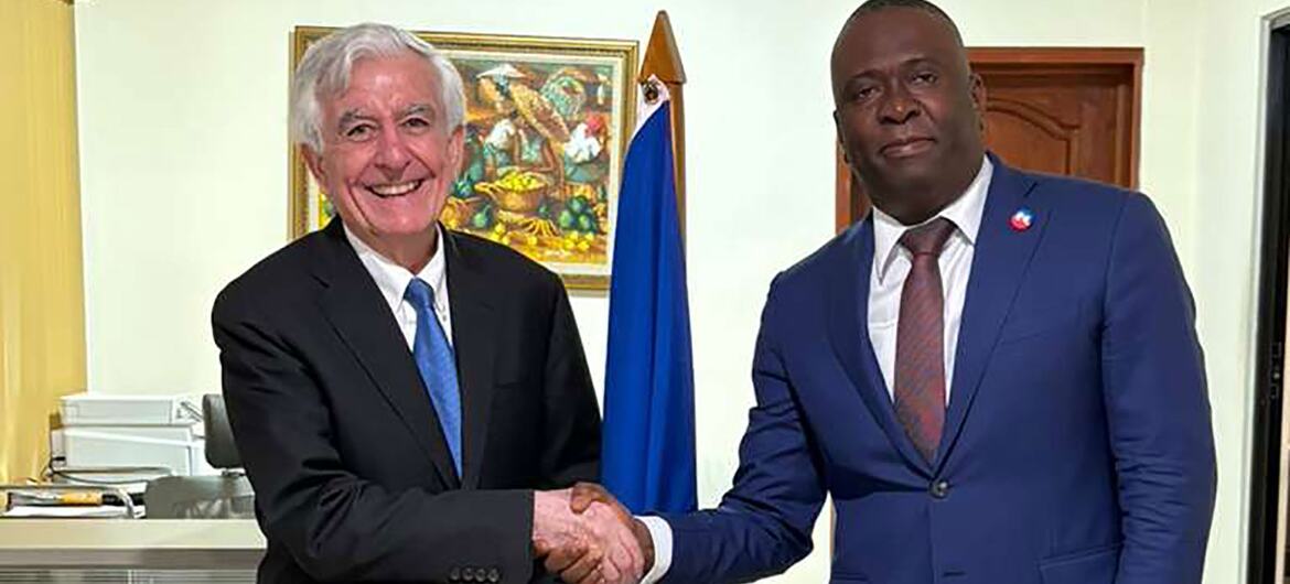 A formal handshake between French diplomat Jean-Yves Le Drian and Haitian official Gabriel Pelissier in an office setting, with the Haitian flag visible in the background.