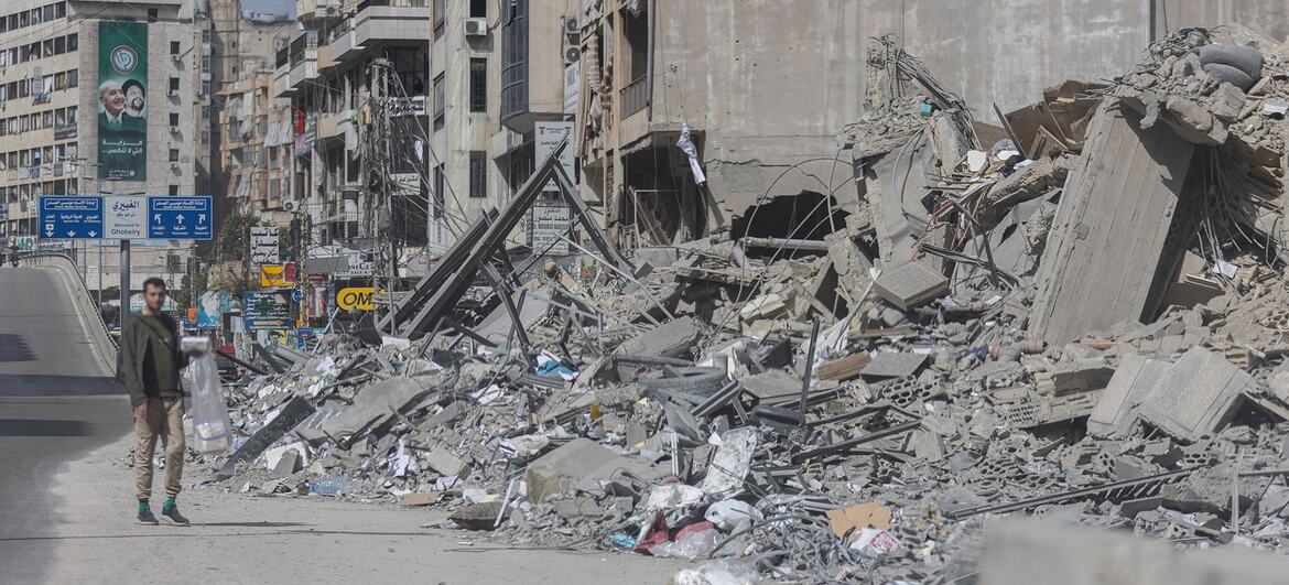 Un edificio gravemente dañado se encuentra en Beirut, Líbano, después de recientes ataques aéreos: escombros y escombros llenan la calle en primer plano donde camina un hombre.