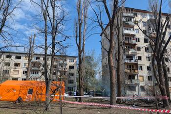 An orange emergency tent stands in front of a damaged apartment building in Ukraine after a missile and drone attack, with caution tape cordoning off the area and debris scattered on the ground.