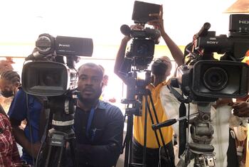 A group of cameramen with professional video cameras on tripods at a press event in Haiti.