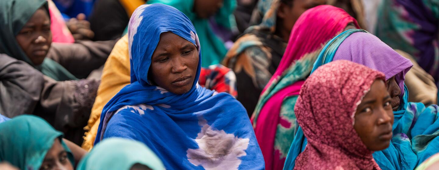 Un groupe de femmes et d'enfants réfugiés soudanais, vêtus de foulards colorés, assis ensemble dans un camp de réfugiés au Tchad, soulignant la crise humanitaire causée par la guerre en cours au Soudan.