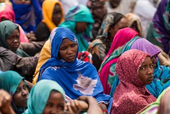 A group of Sudanese refugee women and children, wearing colorful headscarves, sit together in a refugee camp in Chad, highlighting the humanitarian crisis caused by the ongoing war in Sudan.