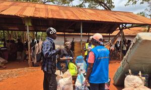 Buchumi Deuline, 58, stands at a departure center in Tanzania, assisted by UNHCR staff, as part of the voluntary repatriation program for Burundian refugees.