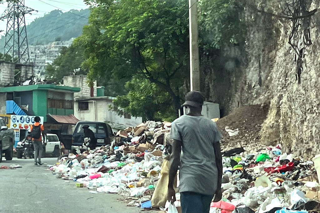 Un hombre camina por una calle de Haití junto a una gran pila de basura y desechos.