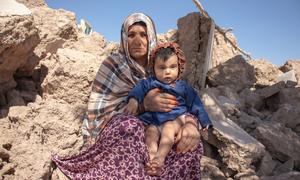 A woman holds a 6-month-old child while sitting in rubble of homes in Afghanistan which were destroyed by an earthquake.