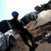 Um soldado de manutenção da paz da ONU , usando capacete azul e uniforme militar, está perto de um veículo branco danificado em um local com destroços no sul do Líbano.