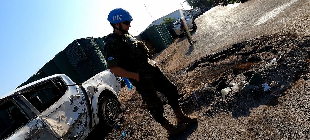 Um soldado de manutenção da paz da ONU , usando capacete azul e uniforme militar, está perto de um veículo branco danificado em um local com destroços no sul do Líbano.