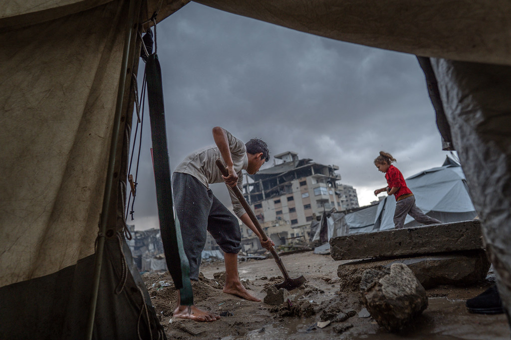 Un niño limpia la entrada de una tienda de campaña tras las fuertes lluvias en Gaza.