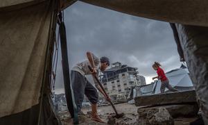 Un niño limpia la entrada de una tienda de campaña tras las fuertes lluvias en Gaza.