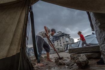 Un niño limpia la entrada de una tienda de campaña tras las fuertes lluvias en Gaza.