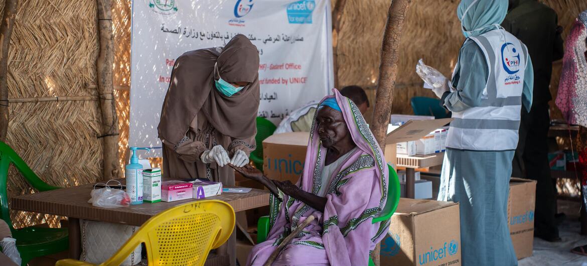 A woman receiving medical care at a UNICEF-supported aid center in Sudan, with staff providing health and nutrition services to displaced families.
