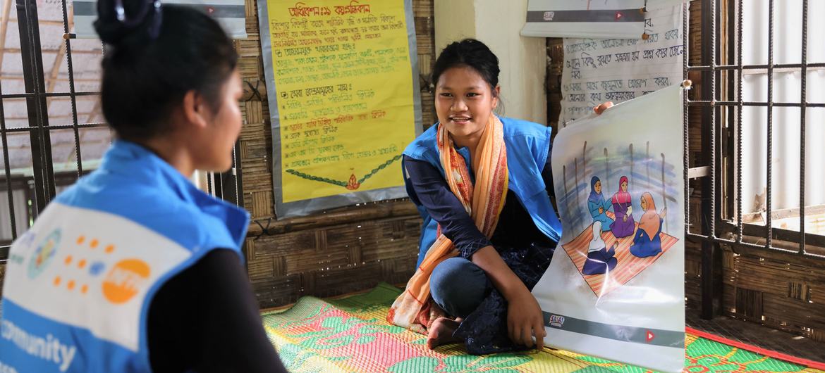 बांग्लादेश में UNFPA की एक सामुदायिक स्वास्थ्य कार्यकर्ता बाल विवाह के बारे में जागरूकता सत्र के दौरान एक युवती को एक शैक्षिक पोस्टर दिखा रही हैं।