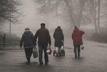 Un grupo de personas, incluida una mujer empujando un cochecito, caminan por una calle de niebla en Chasiv Yar, Ucrania, llevando suministros de ayuda humanitaria proporcionados por ACNUR.
