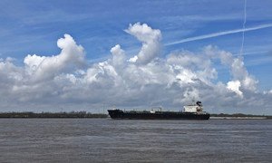 A large cargo ship sailing on the Mississippi River near New Orleans, with a cloudy blue sky above.