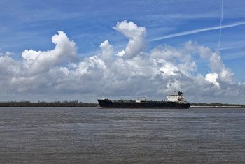 A large cargo ship sailing on the Mississippi River near New Orleans, with a cloudy blue sky above.