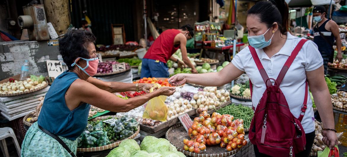 在菲律宾马尼拉的一个市场上，一名蔬菜小贩为顾客服务。