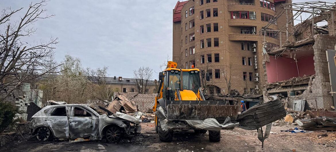 Immeuble résidentiel détruit et voiture brûlée à Dnipro, en Ukraine, avec une excavatrice jaune en train de nettoyer les décombres après une attaque.