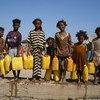 Niños yemeníes desplazados en un asentamiento de Adén sostienen contenedores durante la distribución de agua dos veces al día.