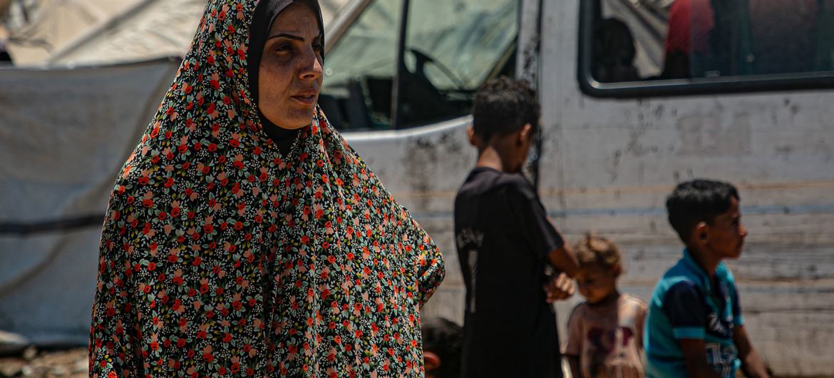 Una mujer palestina y sus hijos en una zona de desplazados en Gaza, con un camión cisterna al fondo.