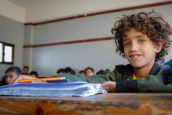 يجلس صبي صغير على مكتب في فصل دراسي، ممسكاً بقلم رصاص وينظر إلى الكاميرا.
