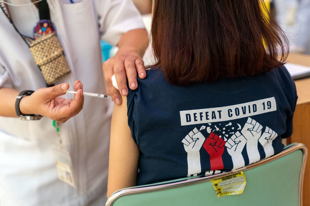 Una chica recibe la vacuna contra el COVID-19 en Filipinas, con una camiseta con el mensaje "Derrotar el COVID-19"