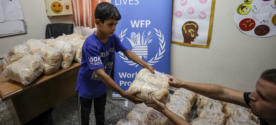 在加沙的一个庇护所里，一名男孩从世界粮食计划署领取到面包。