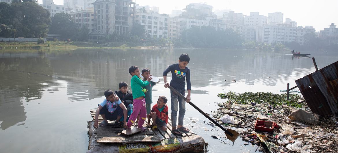 Des enfants traversent un lac pollué sur un radeau de fortune dans le bidonville de Korail, à Dhaka, au Bangladesh.