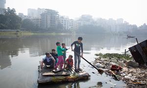 Children cross a polluted lake on a homemade raft in the Korail slum of Dhaka, Bangladesh.