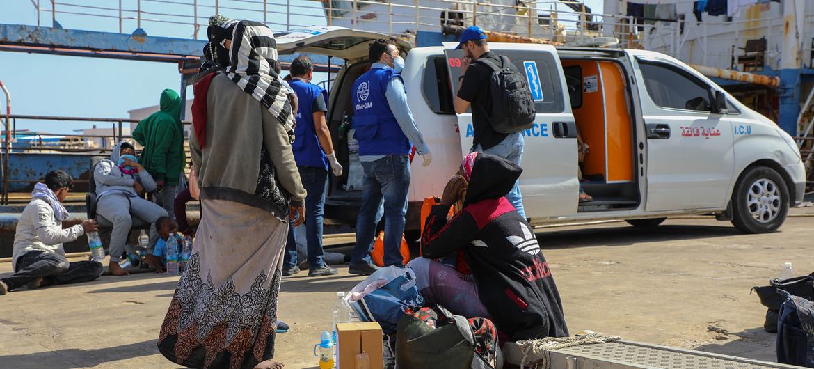 Los trabajadores humanitarios de la OIM ayudan a los migrantes y refugiados en un puerto libio, cargándolos en una furgoneta blanca marcada con el logotipo de la ICU.