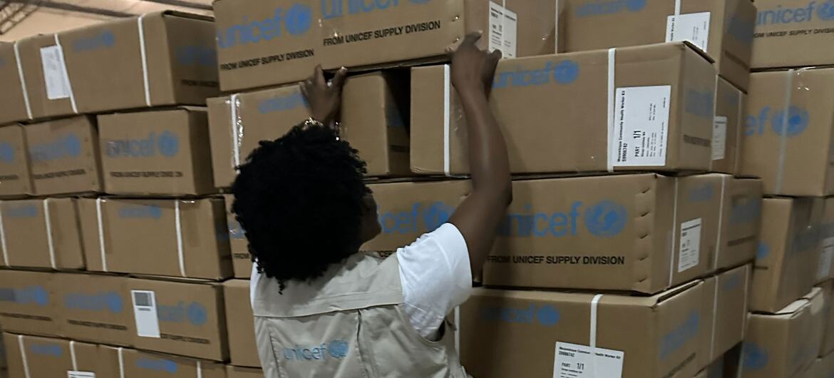 Um membro da equipe da UNICEF empilha caixas de ajuda de emergência em um armazém na província de Gaza, Moçambique, em resposta às inundações causadas pela mudança climática.