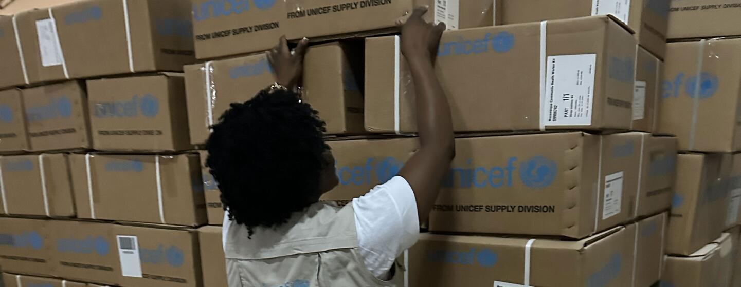 Um membro da equipe da UNICEF empilha caixas de ajuda de emergência em um armazém na província de Gaza, Moçambique, em resposta às inundações causadas pela mudança climática.