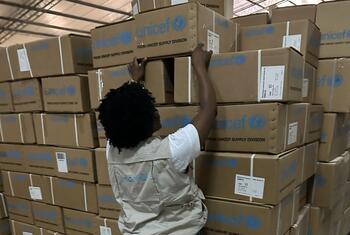 Um membro da equipe da UNICEF empilha caixas de ajuda de emergência em um armazém na província de Gaza, Moçambique, em resposta às inundações causadas pela mudança climática.