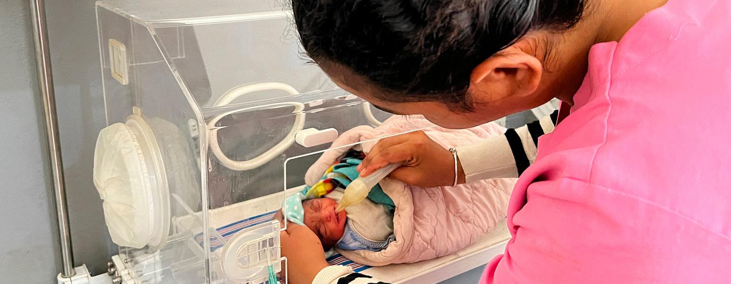 A premature baby is fed in a hospital incubator.
