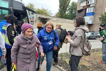 Una mujer de edad avanzada está siendo asistida por otra que lleva un chaleco azul del ACNUR en un centro de tránsito en Járkov, Ucrania.