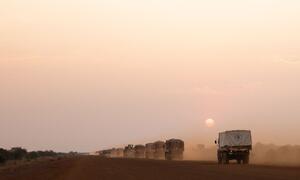 A convoy of World Food Programme trucks carrying 750-800 tons of food departs from Bor, South Sudan, traveling 215km under a hazy sunset. This pre-positioning mission is crucial for efficient aid delivery in a region with poor road conditions and security challenges.
