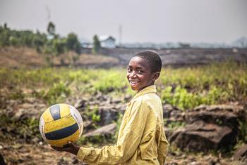Un garçon souriant, vêtu d'un t-shirt jaune, tient un ballon de volley-ball dans un espace adapté aux enfants soutenu par l'UNICEF en République démocratique du Congo.