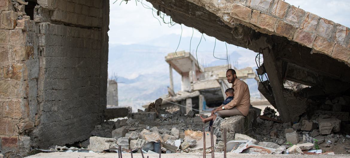 A father holds his child amid the rubble of a destroyed house in Taiz city, Yemen.