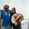 Mfanyakazi wa UNHCR mwenye tabasamu akiwa amevaa fulana ya bluu amesimama na mwanamke aliyekimbia makazi yake akiwa ameshika kifurushi ndani ya hema jeupe katika eneo la kukusanyika la wakimbizi wa ndani nchini Sudan.