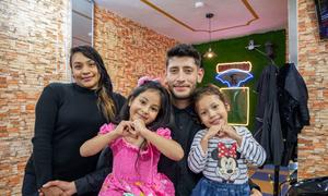 A Venezuelan refugee poses with his family in his new barbershop in Ecuador. 