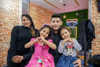 A Venezuelan refugee poses with his family in his new barbershop in Ecuador. 
