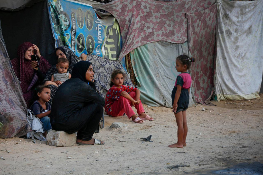 Des femmes et des enfants déplacés sont assis et debout dans un camp de tentes de fortune à Gaza.