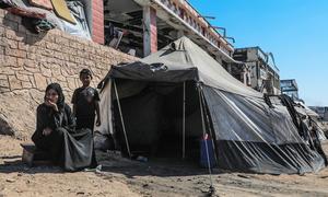 Una familia desplazada en Gaza frente a la tienda de campaña en la que se refugia.