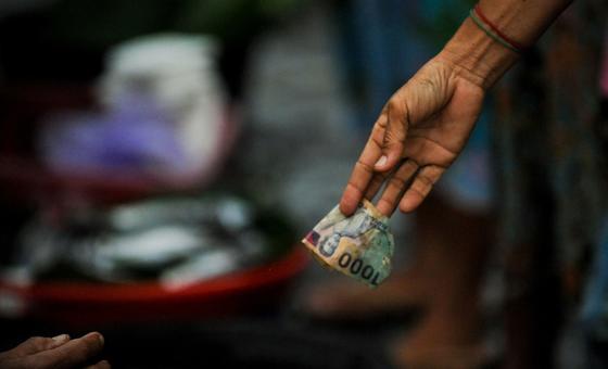 انڈونیشیا میں ایک بازار میں لین دین کے دوران ایک خاتون کے ہاتھ میں 1000 روپے کا نوٹ ہے۔