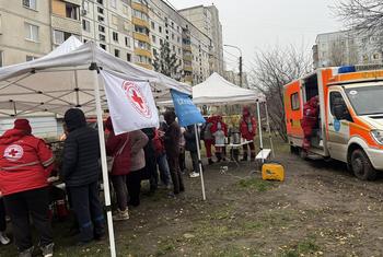 身穿红色制服的人道主义援助人员和红十字会帐篷正在为城区民众提供援助。附近停着一辆救护车。